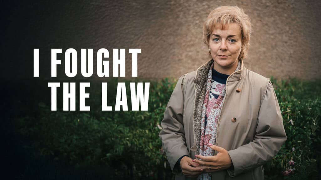 Sheridan Smith as Ann Ming in ITV’s I Fought the Law, standing outside in a beige coat with the series title displayed beside her.